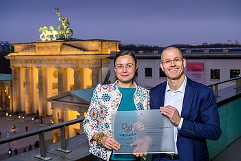 Zwei Personen vor dem Brandenburger Tor mit einem Vielfalt-Zertifikat